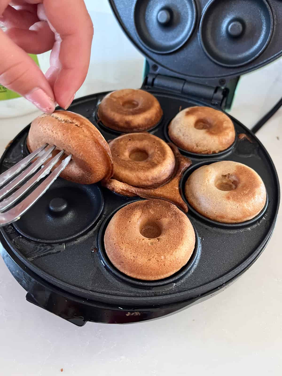 Pulling a cooked donut out of a donut maker with a fork.