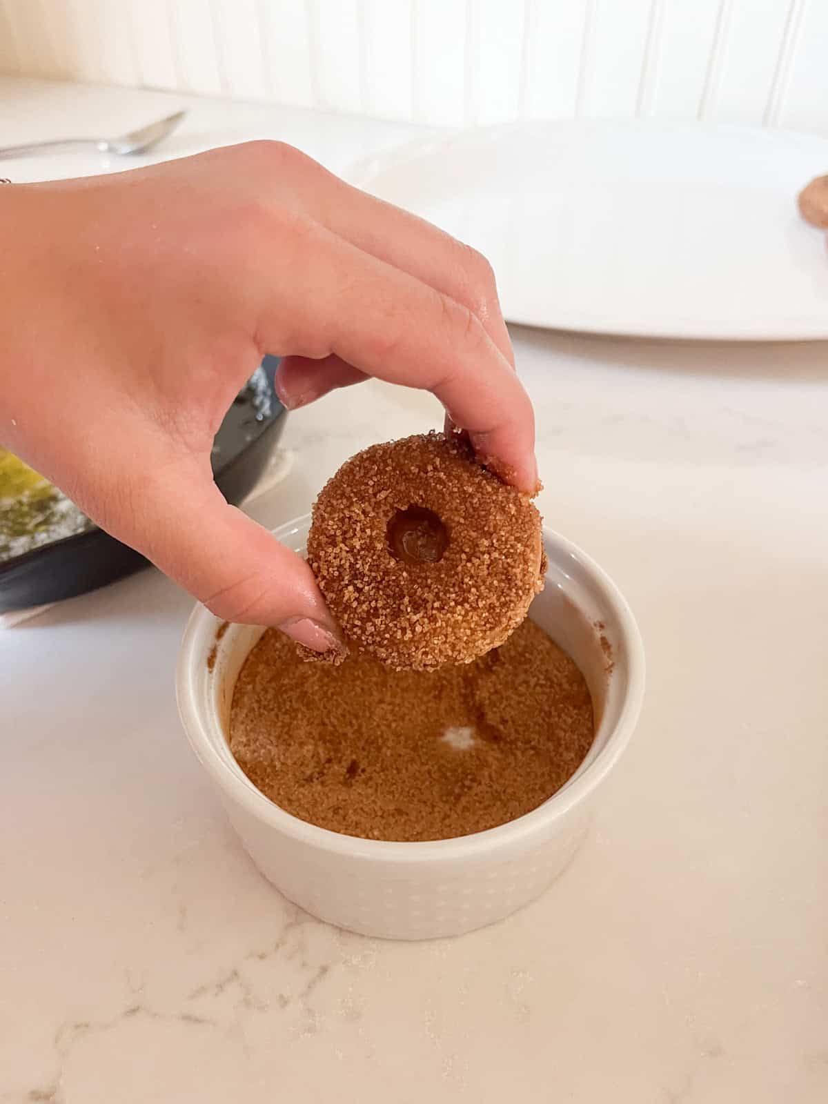 Dipping homemade apple cider donuts in a bowl of cinnamon sugar.