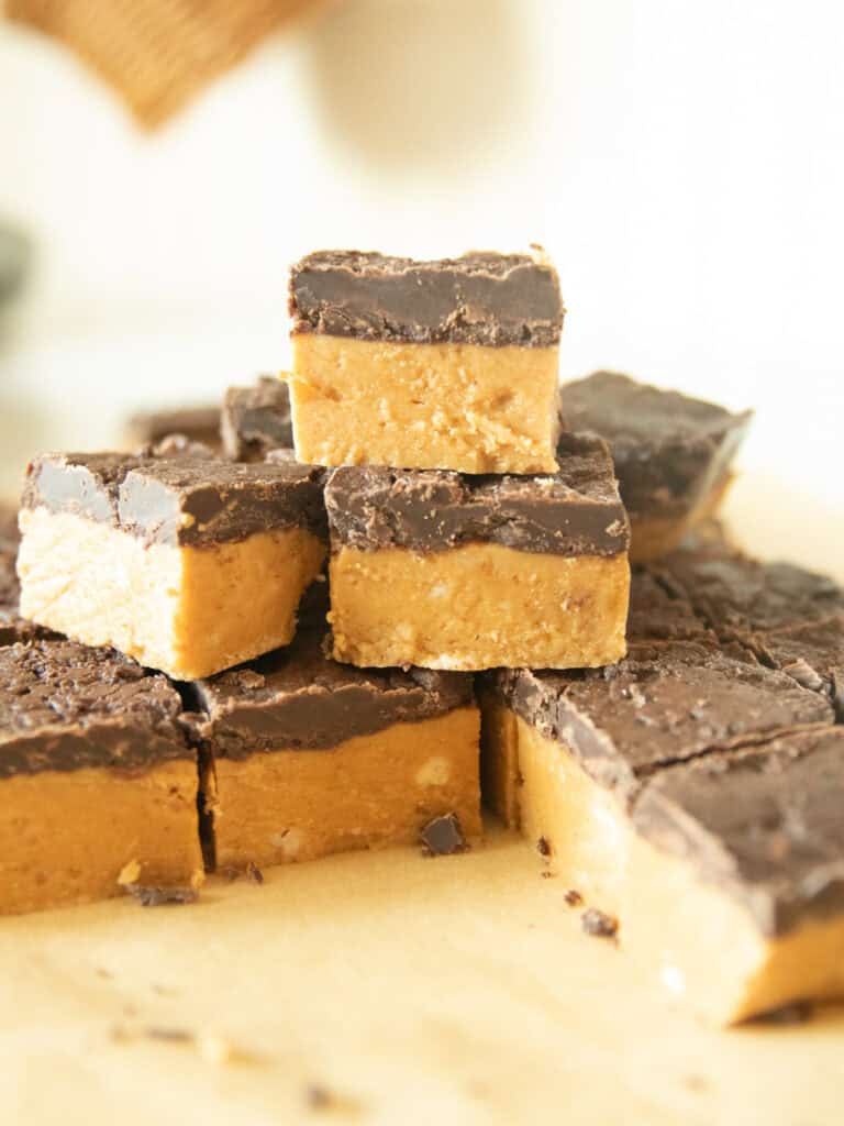 No bake peanut butter chocolate bars stacked in a pile on a wooden surface.