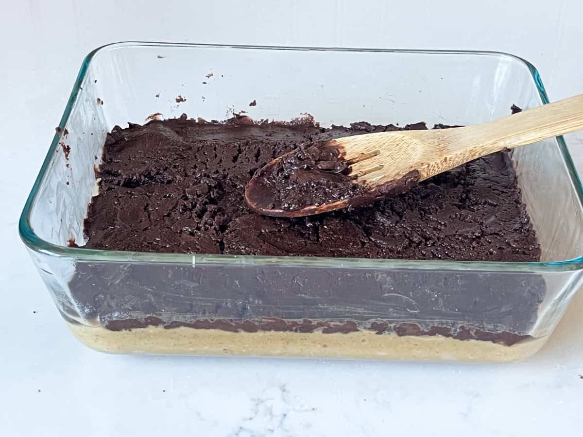 Spreading chocolate mixture on top of peanut butter mixture in a baking dish.