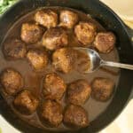 Scooping a meatball with gravy out of a cast iron skillet.