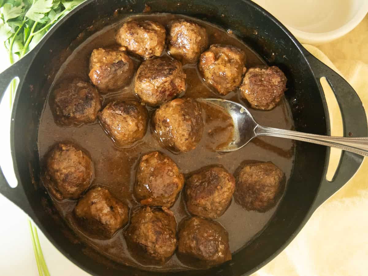 Scooping a meatball with gravy out of a cast iron skillet.
