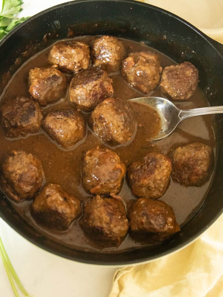 Venison meatballs swimming in brown gravy in a cast iron skillet with a spoon.