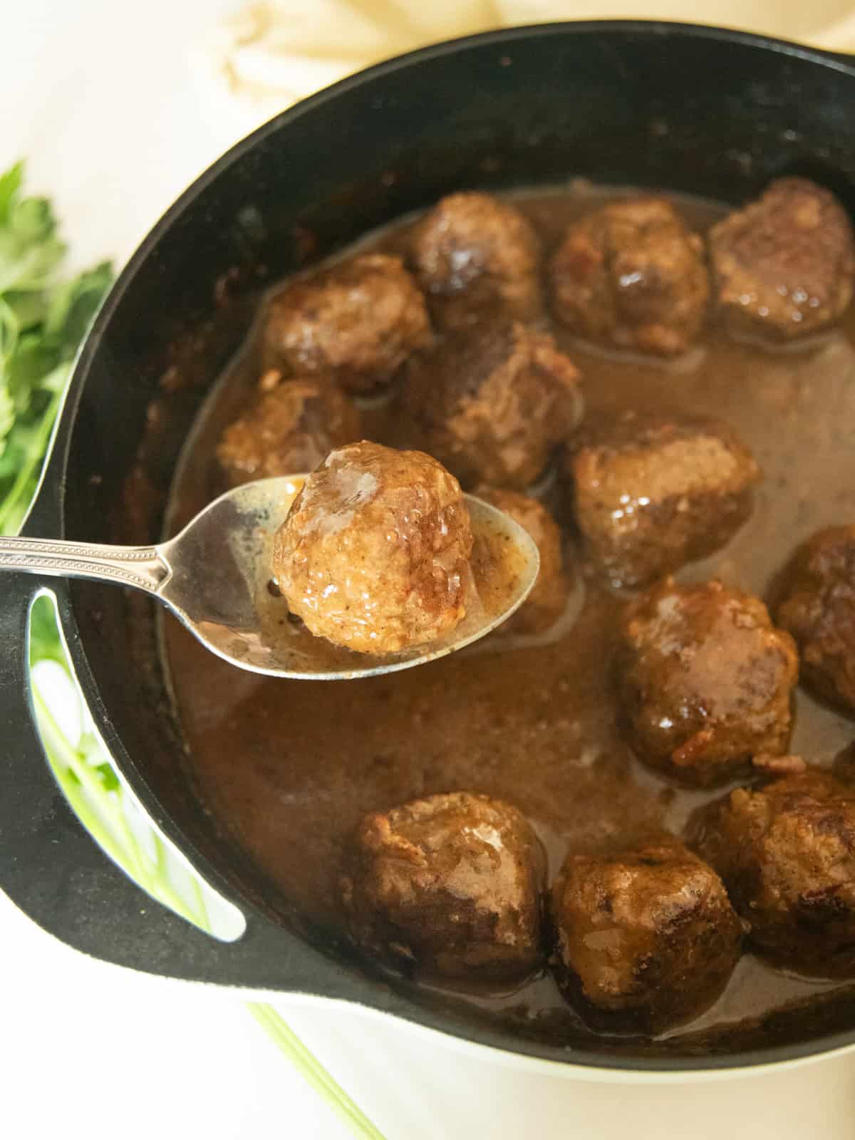 Scooping a meatball out of a cast iron skillet with a spoon.