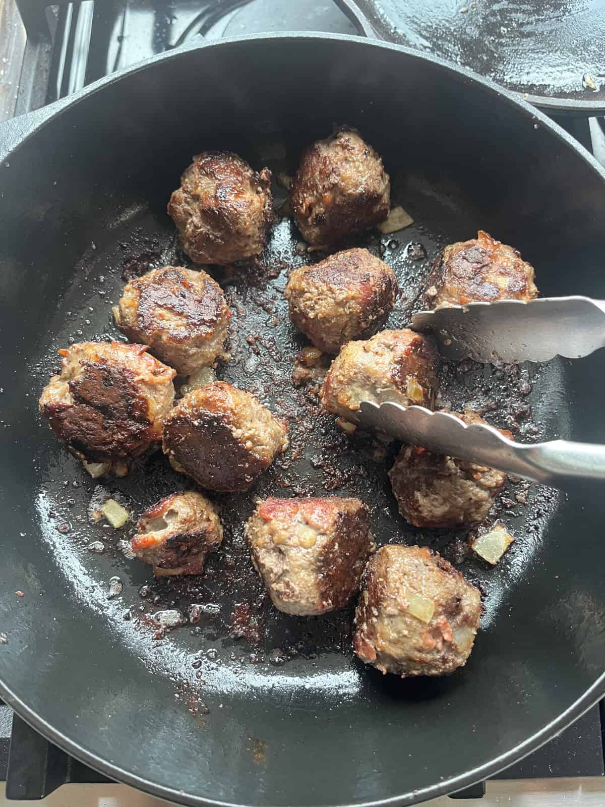 Browning meatballs in a cast iron skillet with tongs.