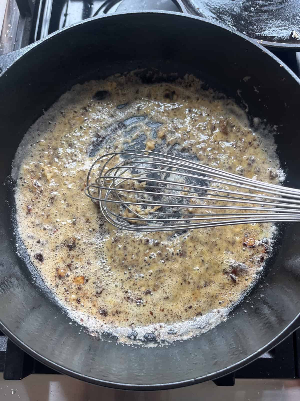 Whisking a roux in a cast iron skillet.