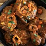 Braised osso buco in a cast iron skillet with a wooden spoon.