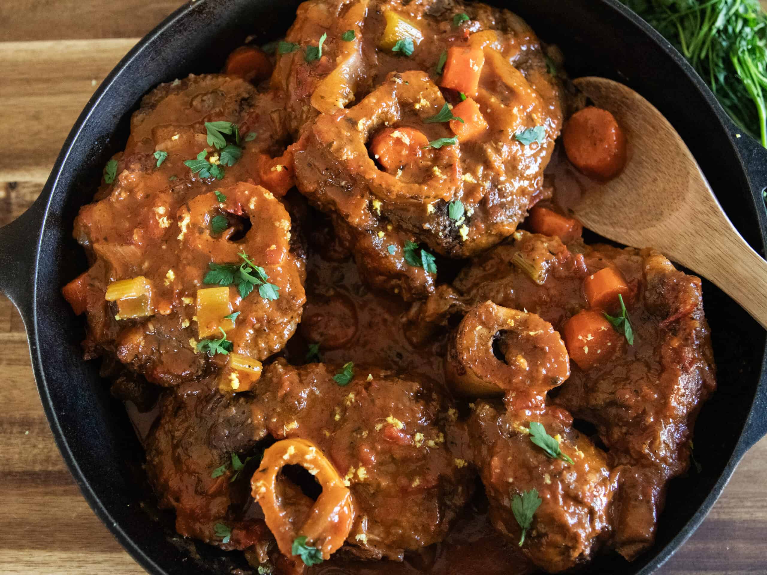 Braised osso buco in a cast iron skillet with a wooden spoon.