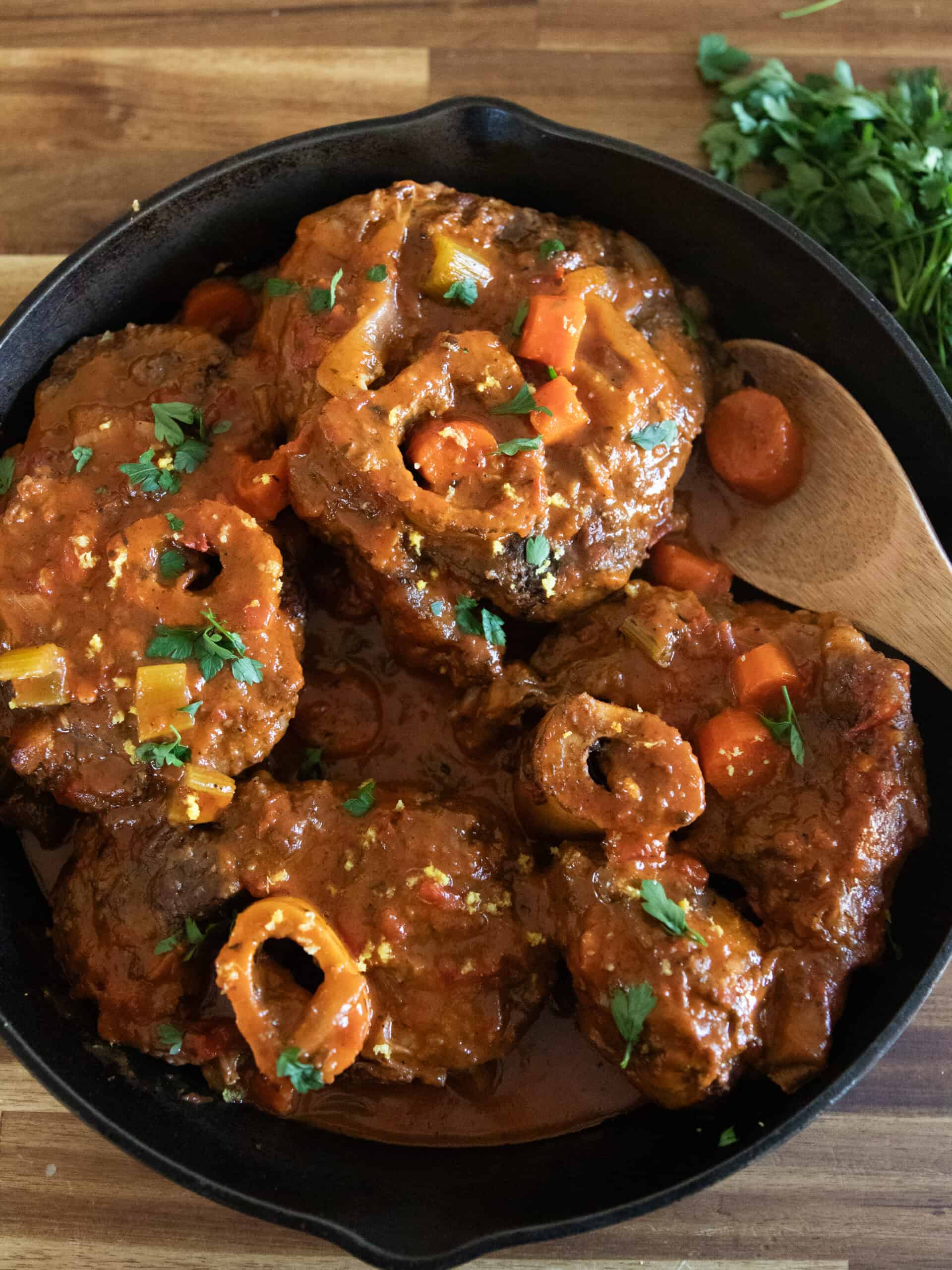 Beef osso buco in a cast iron skillet with a wooden spoon.