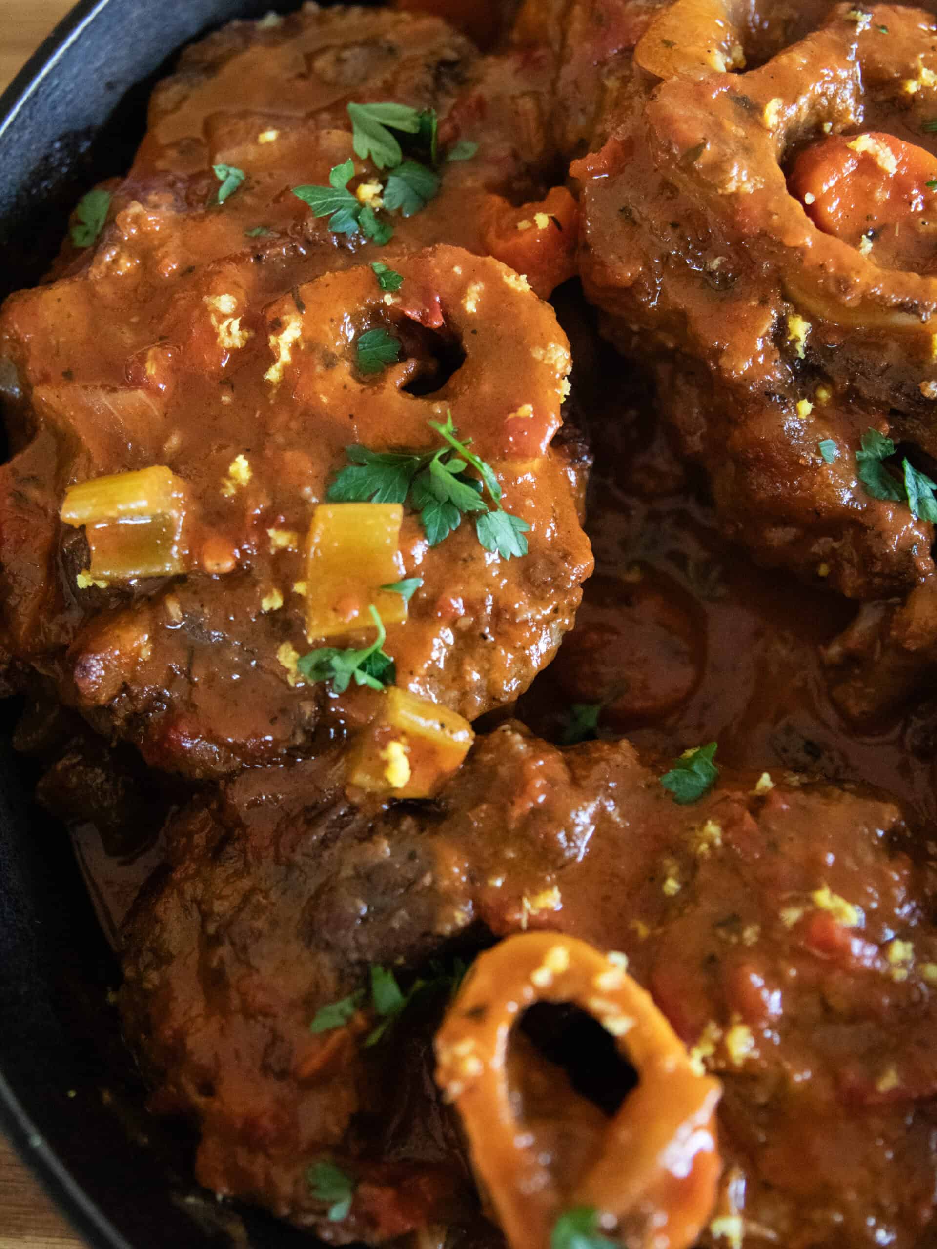 A close-up of beef osso buco in a cast iron skillet.