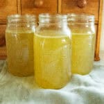Three jars of homemade chicken broth on a blue towel.