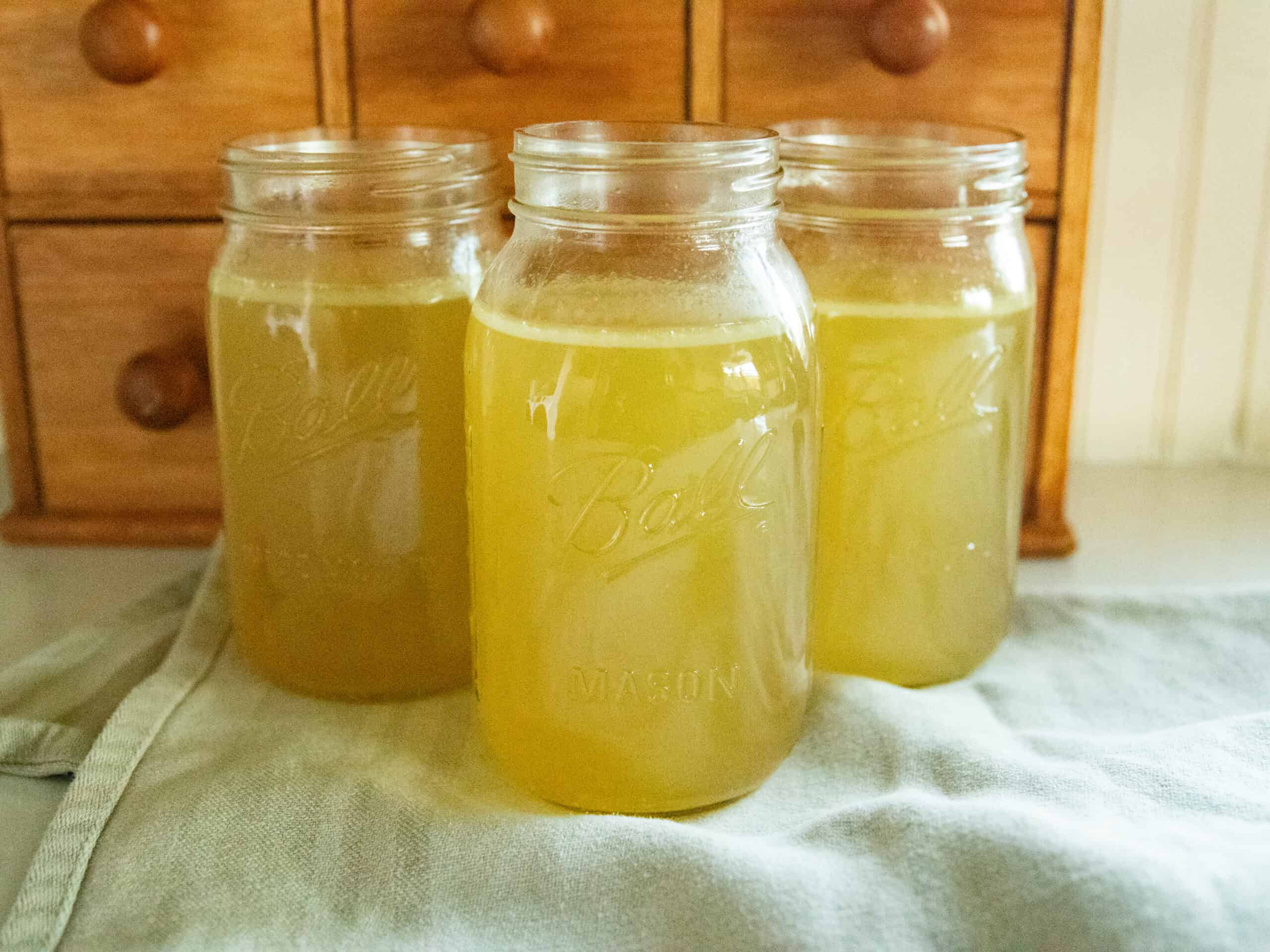 Three jars of homemade chicken broth on a blue towel.