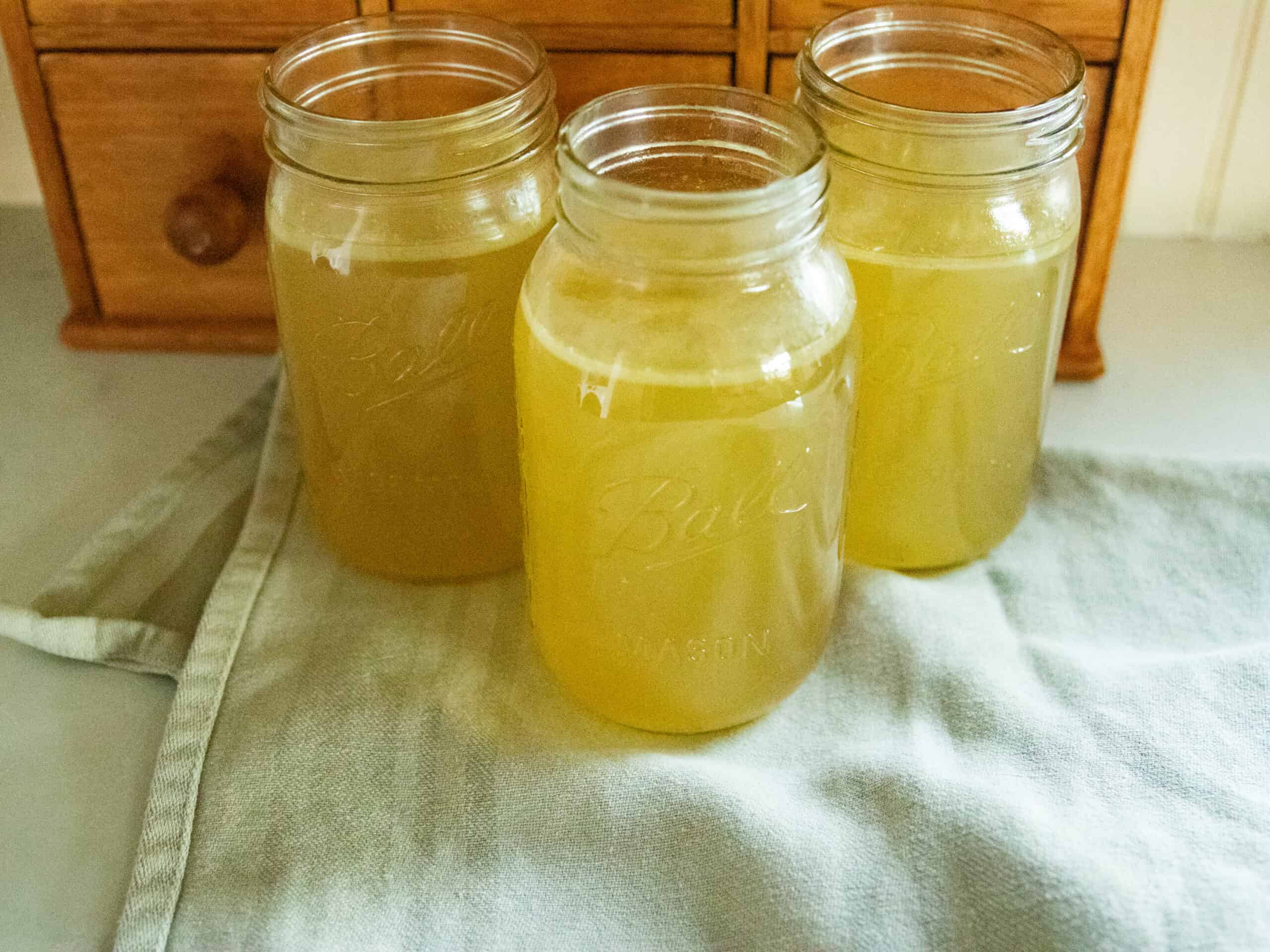 Three jars of homemade chicken broth on a blue towel.