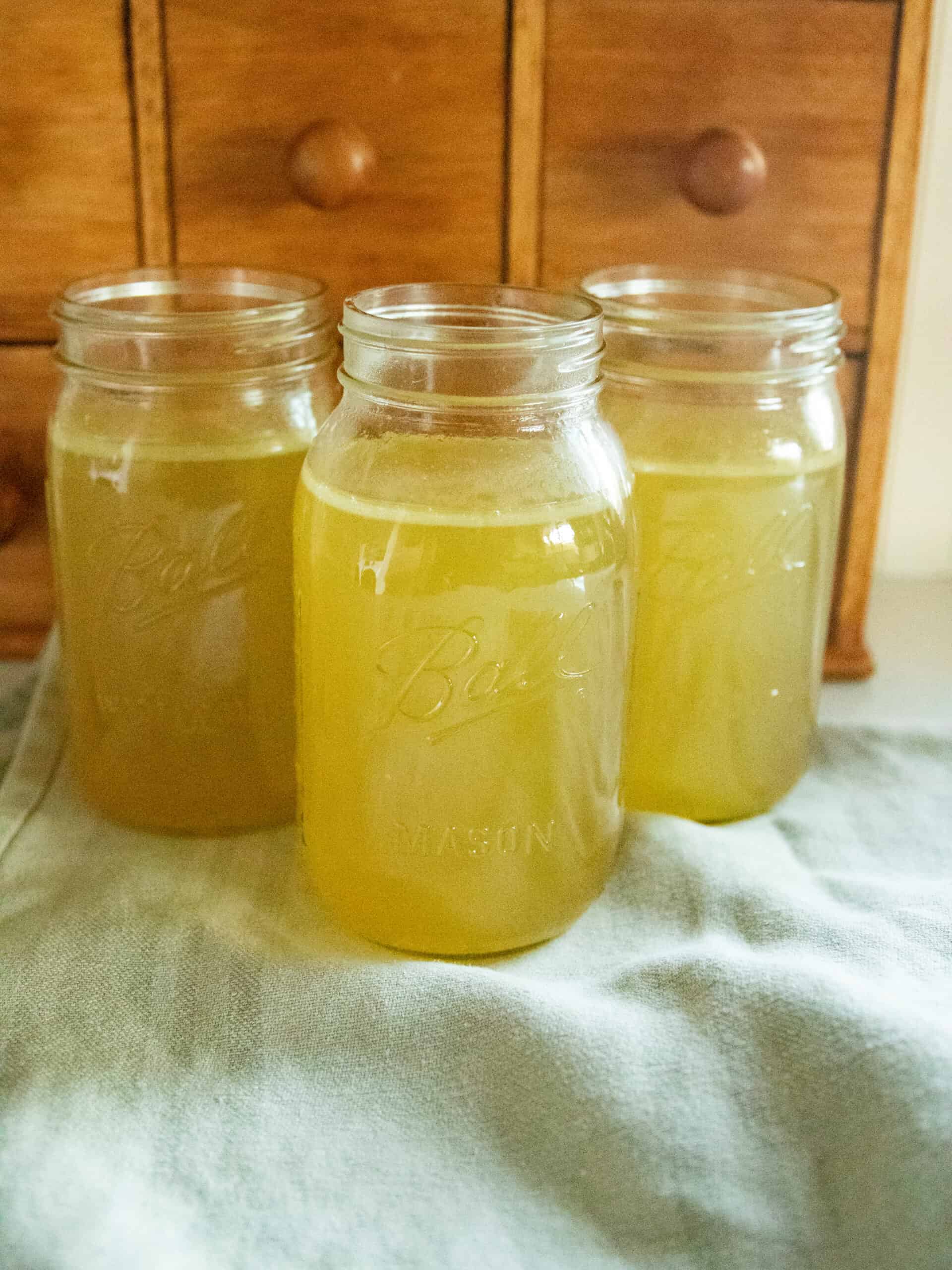 Three jars of chicken broth on a blue towel.