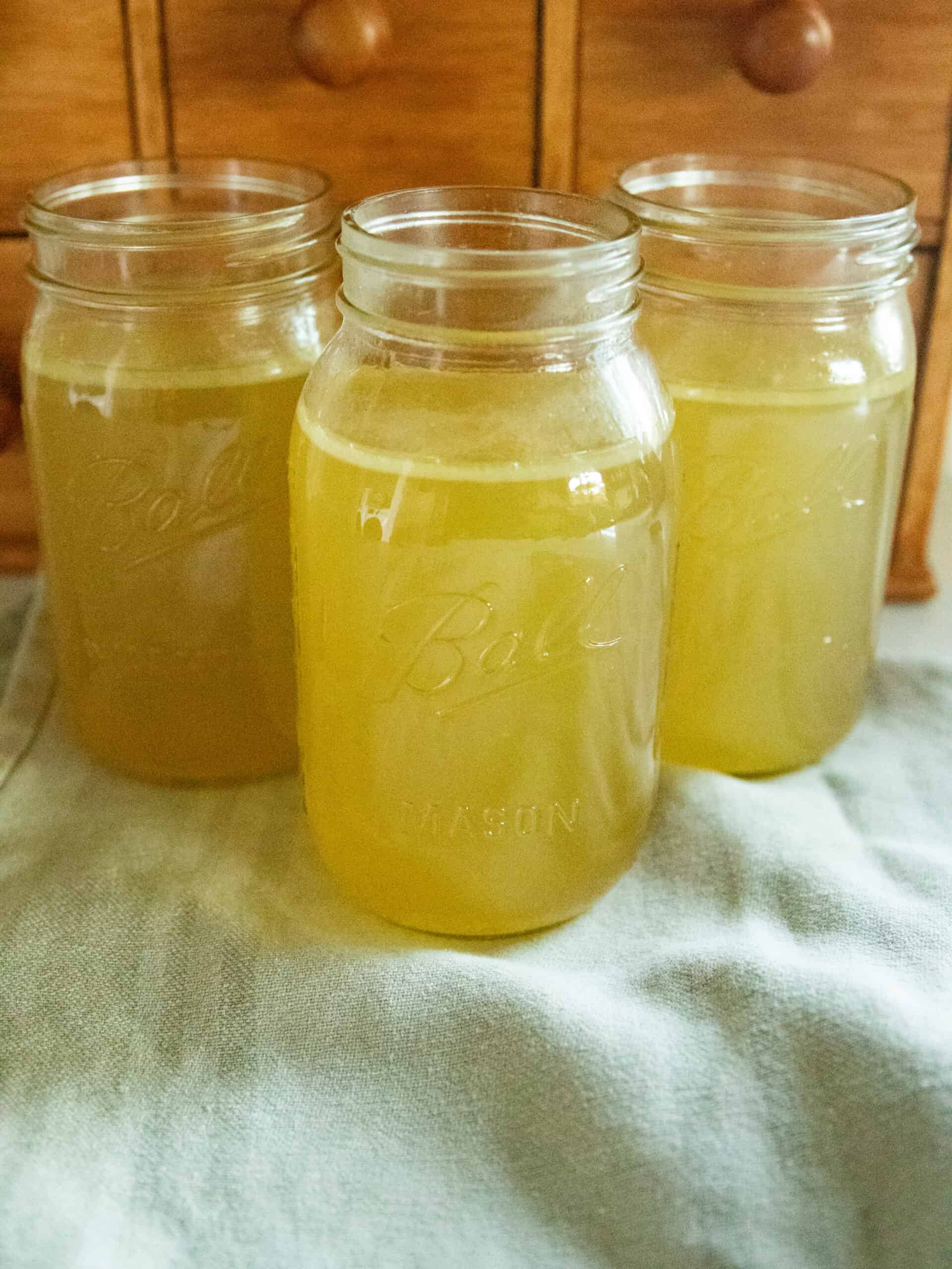 Three jars of homemade chicken broth on a blue towel.