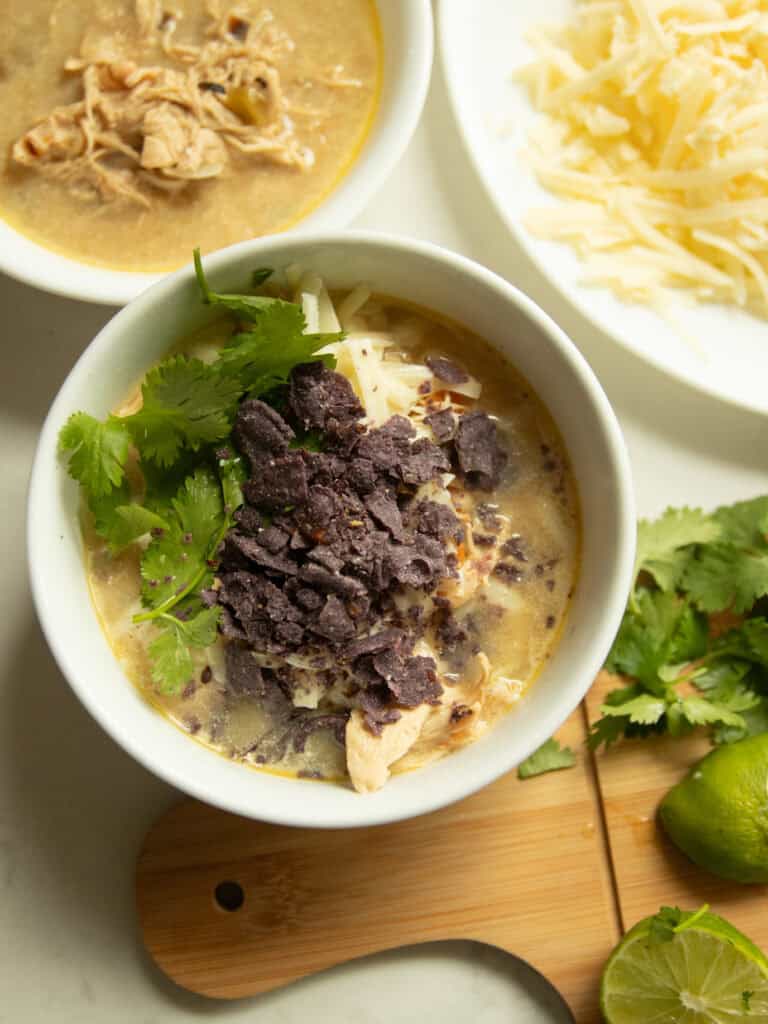 A bowl of white chicken chili with bowls of toppings surrounding it.