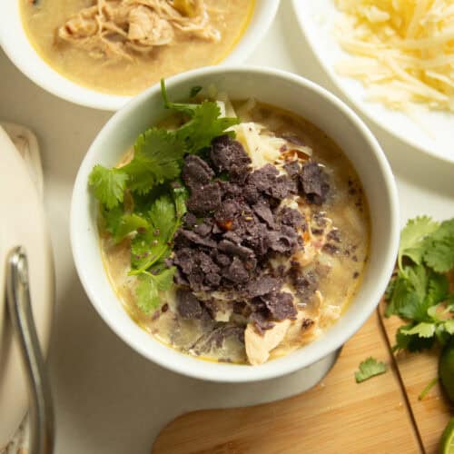 A bowl of white chicken chili with toppings and another bowl surrounding it.