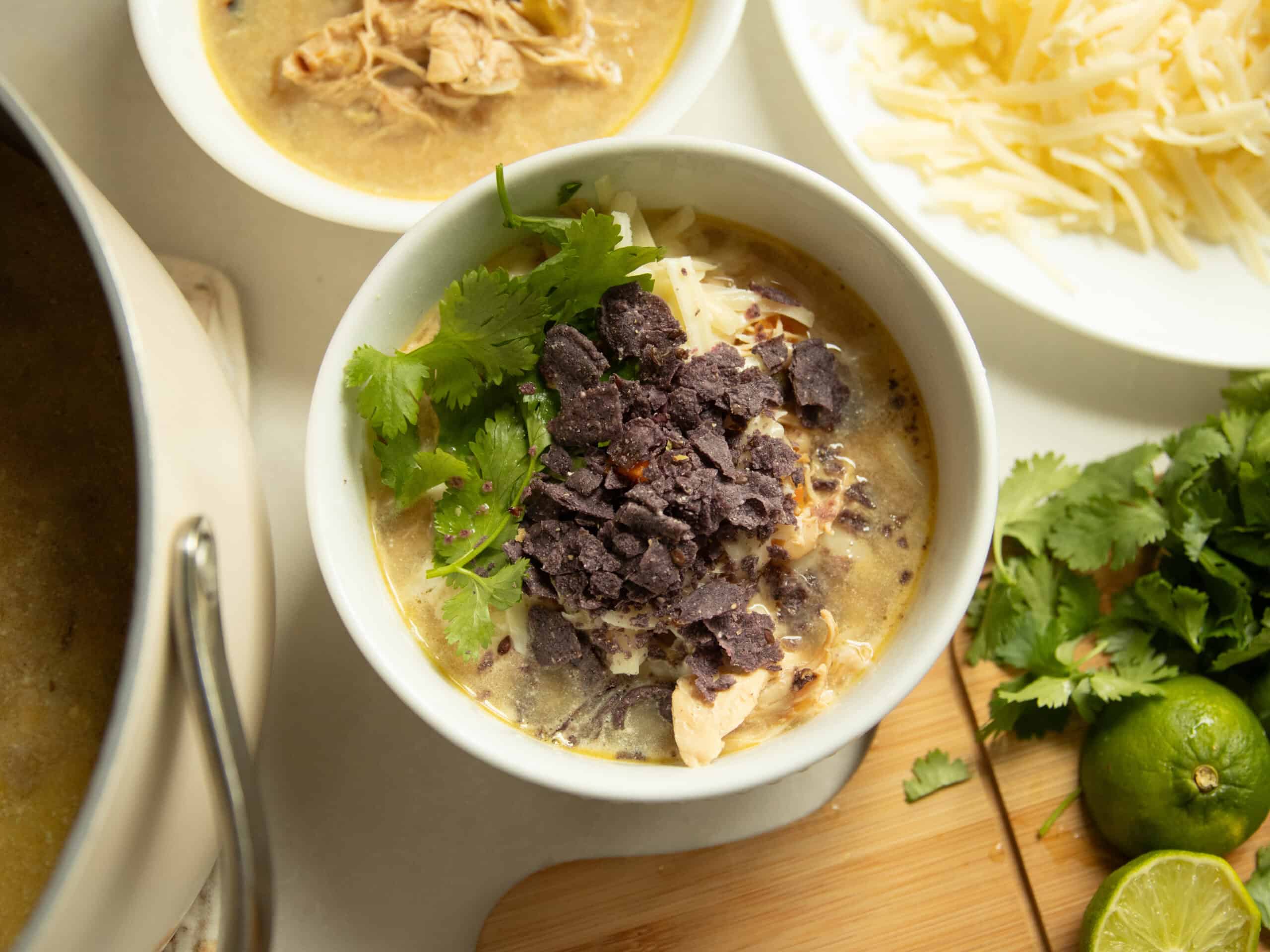 A bowl of white chicken chili with toppings and another bowl surrounding it.