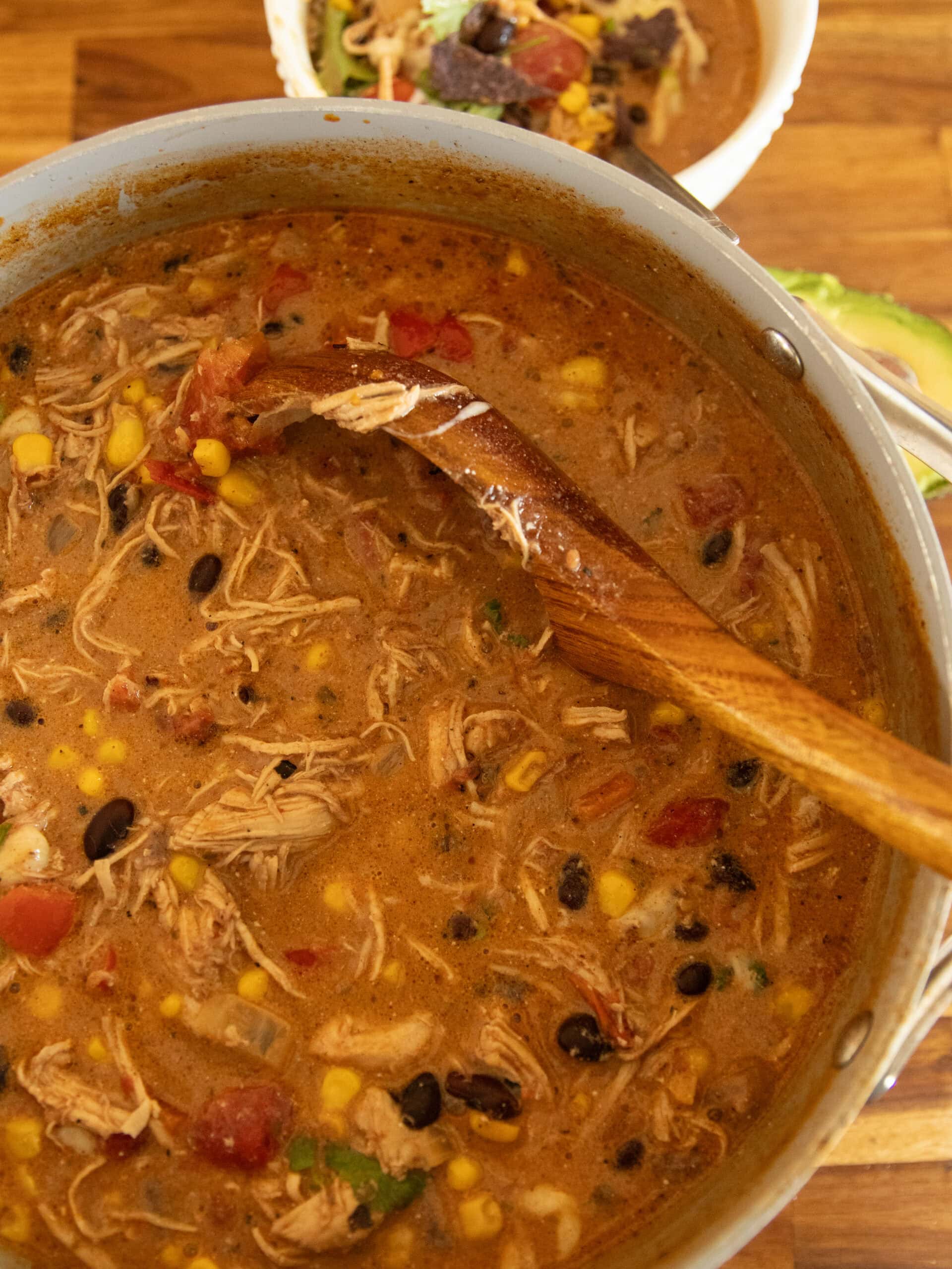 Scooping tortilla soup out of a pot with a bowl of soup next to it.