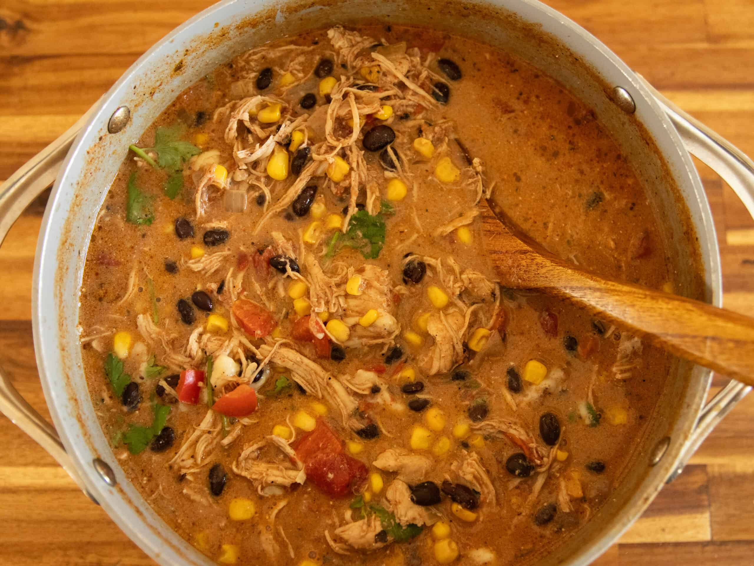 A pot of creamy chicken tortilla soup with a wooden ladel.