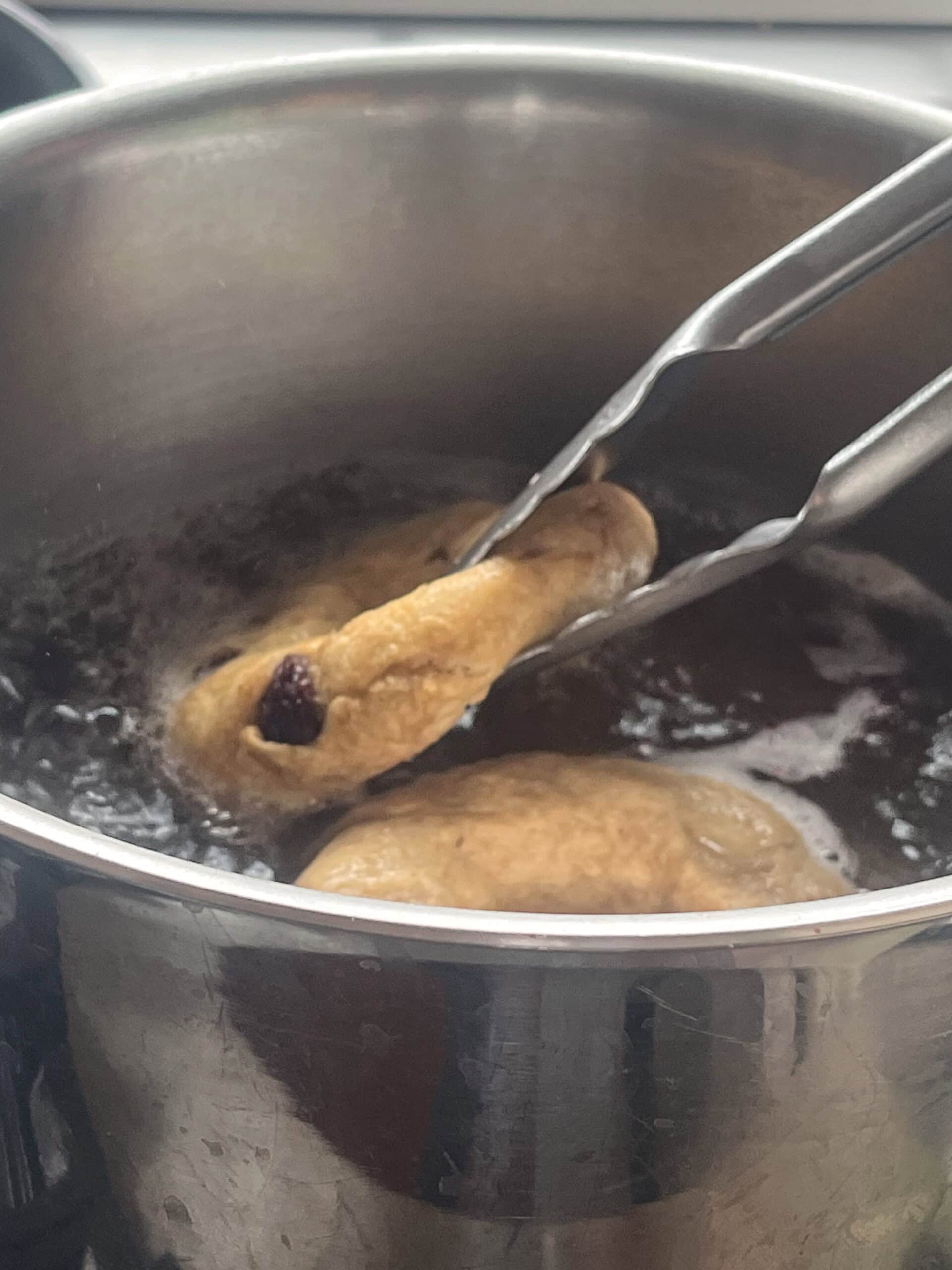 Boiling bagels in a pot of water, flipping with tongs.